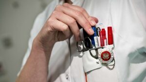 Sygeplejersker sætter kuglepen fast i brystlommen, hvor sygeplejeremblemet er synligt . DSR er medlem af Fagbevægelsens Hovedorganisation