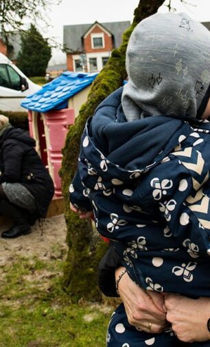 Barn får et knus af en pædagog på legepladsen. Fagbevægelsens Hovedorganisation