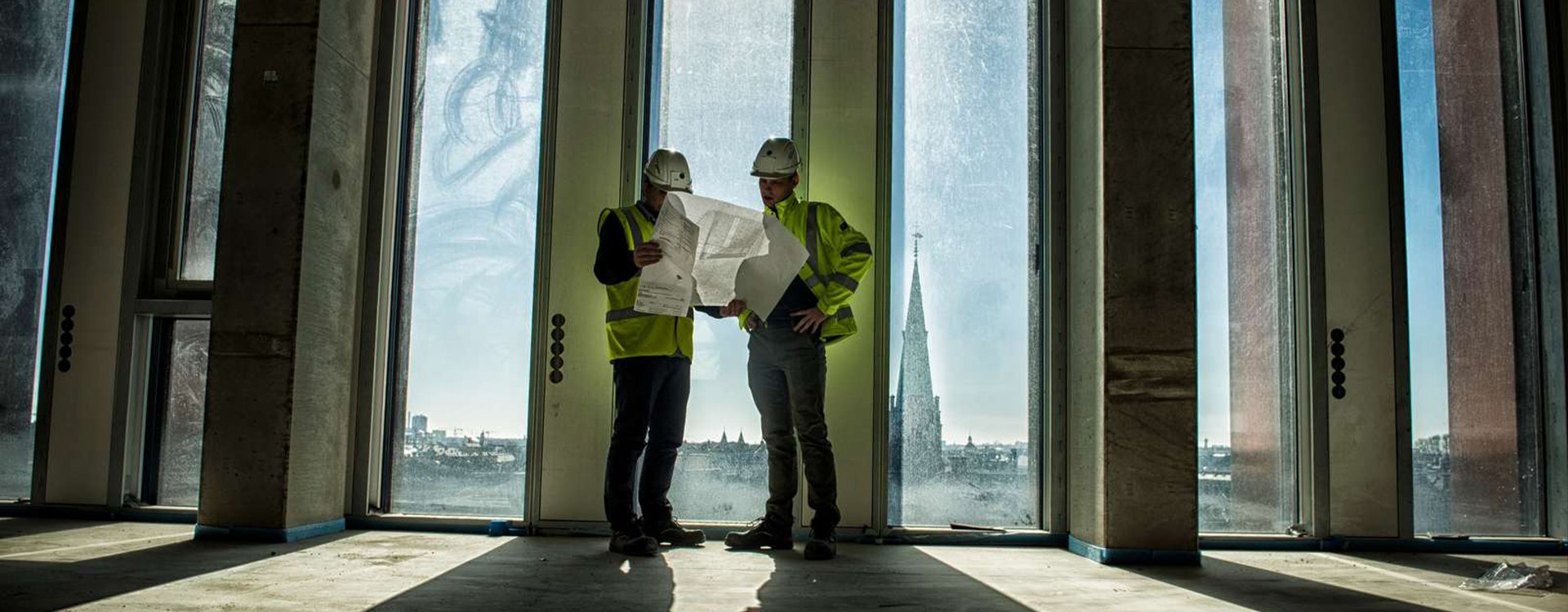 Fagbevægelsens Hovedorganisation, 2 byggekonstruktører kigger på tegninger sammen på byggeplads højt oppe med flot klar udsigt, Ludvigsen