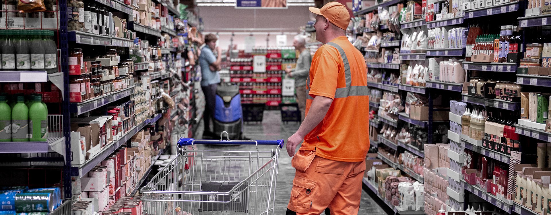 Mand i orange arbejdstøj med indkøbsvogn i supermarked