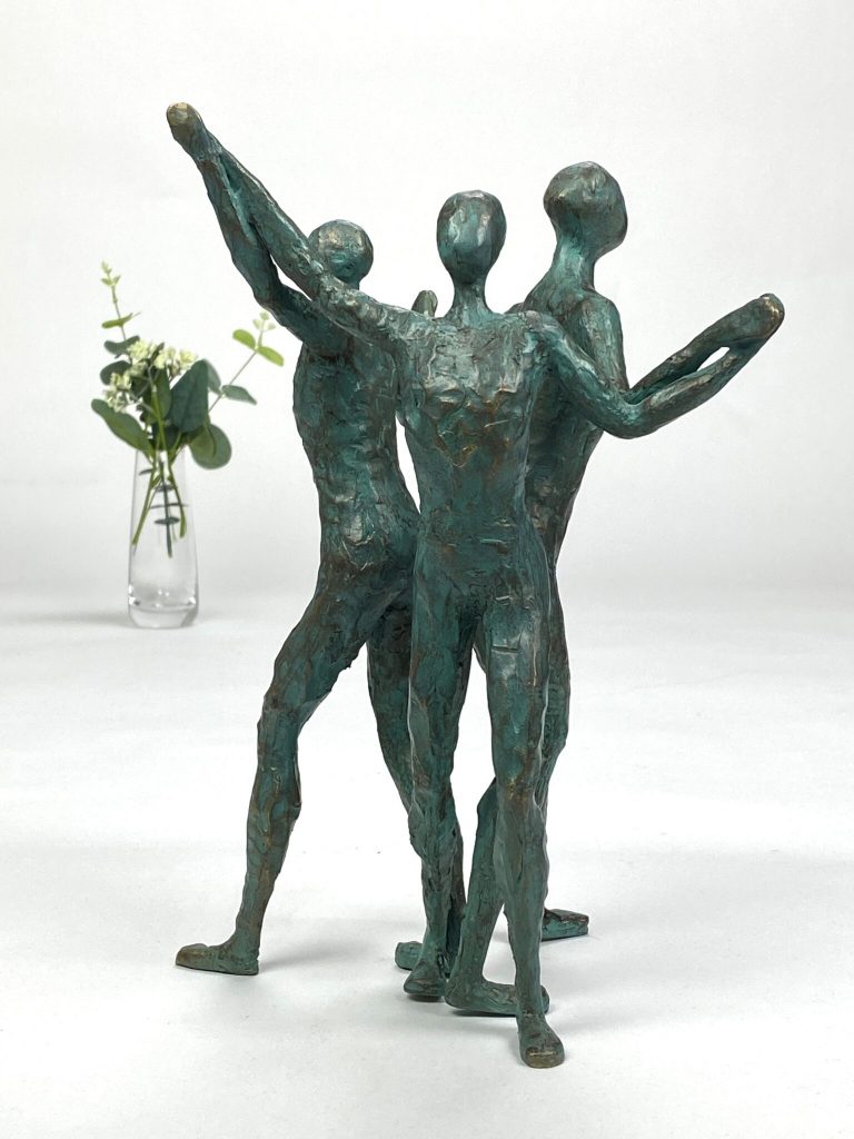 Skulptur af tre figurer med opstrakte arme der holder hinanden i hænderne